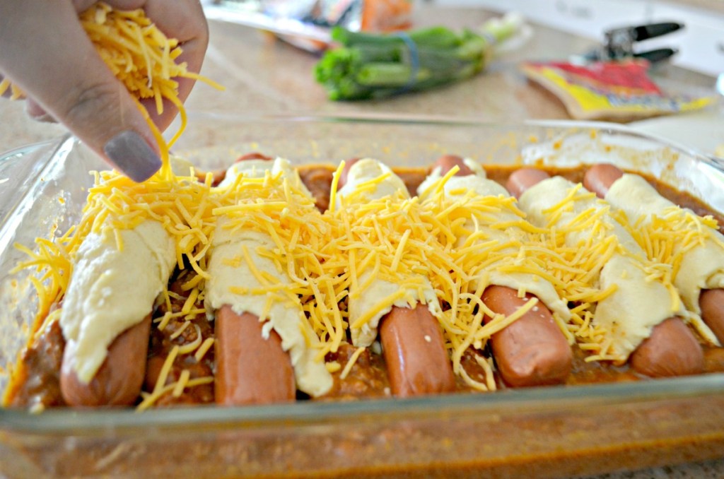 sprinkling cheese on top of baked chili dogs