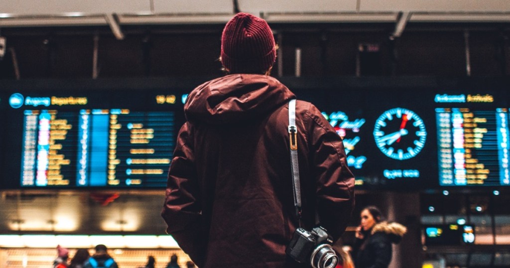 person standing in front of airport departures and arrivals screen