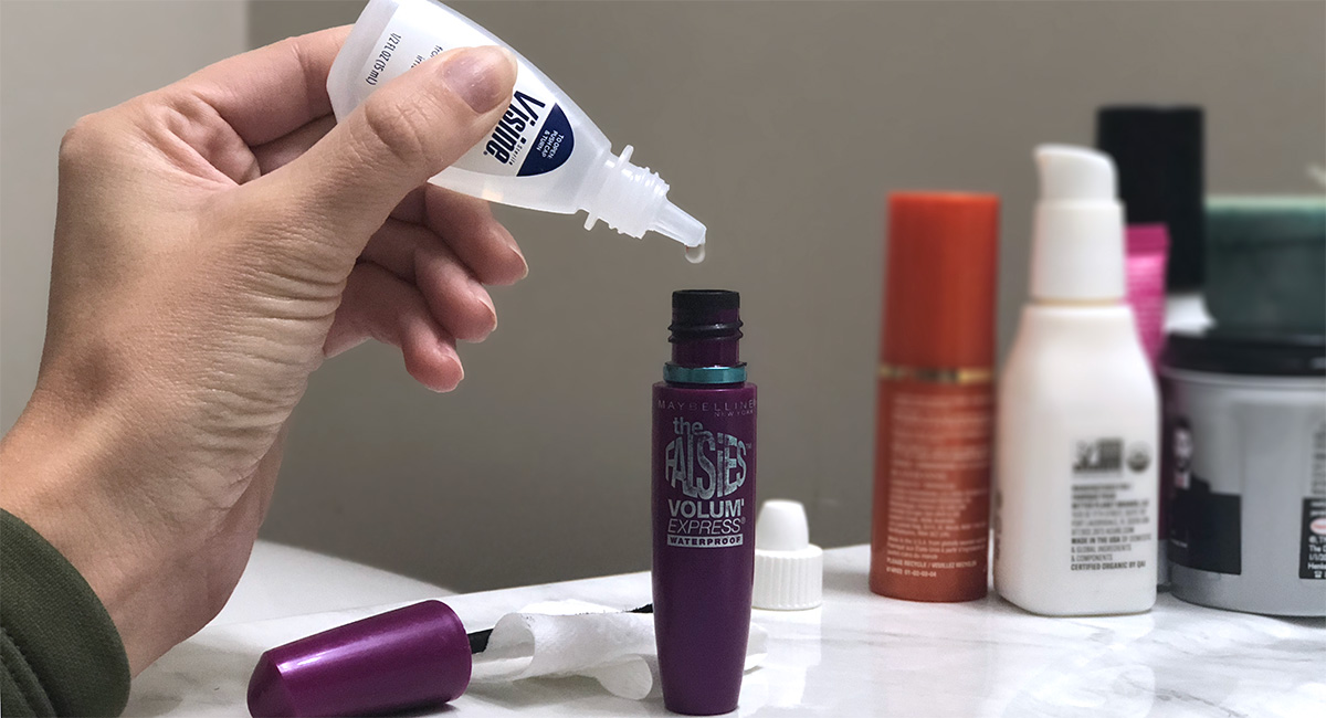 hand holding dropper bottle of eyedrops putting into purple mascara bottle