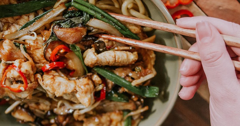 hand using chop sticks to eat Asian food