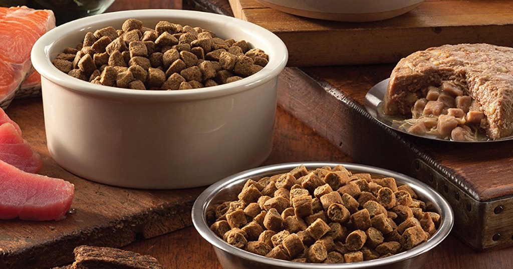 multiple dog food dishes filled with dog food next to fresh meat and fish