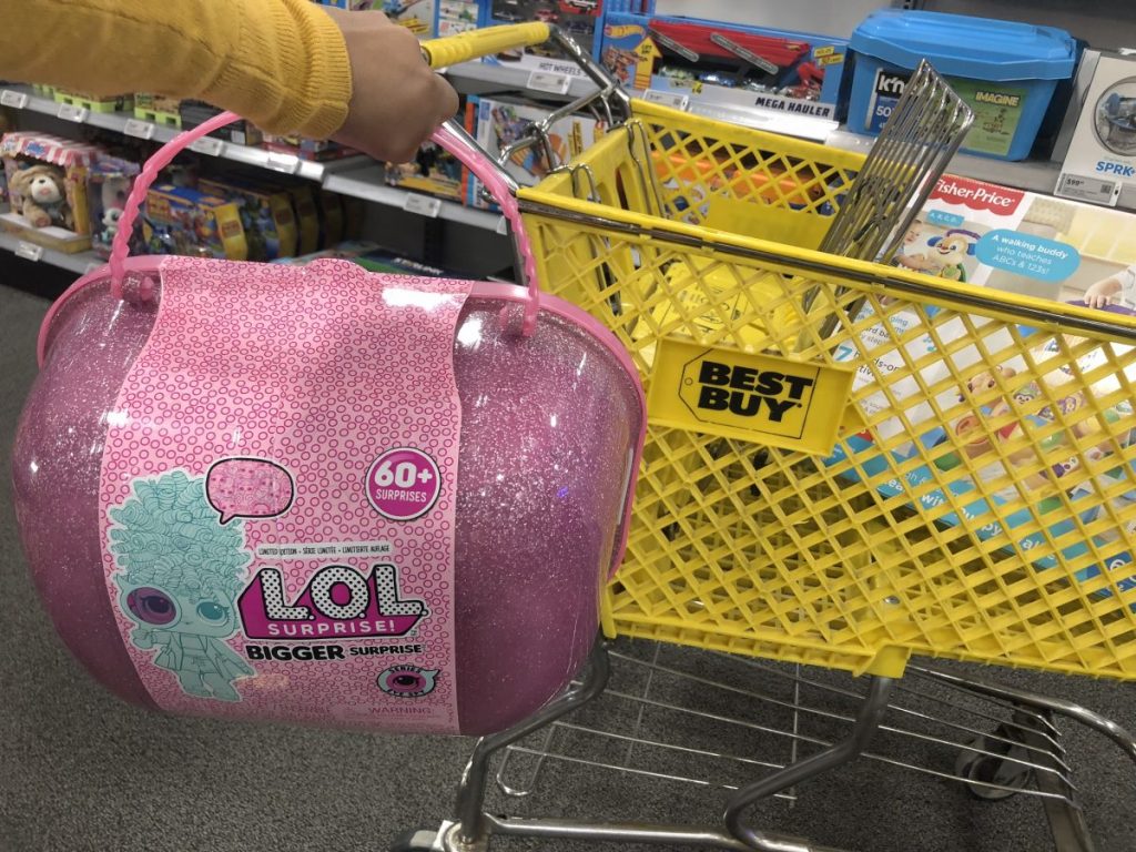 hand holding pink toy in front of shopping cart