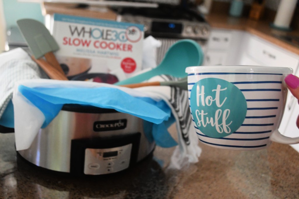 Hand holding Crock pot gift basket fillers like a Hot Stuff mug