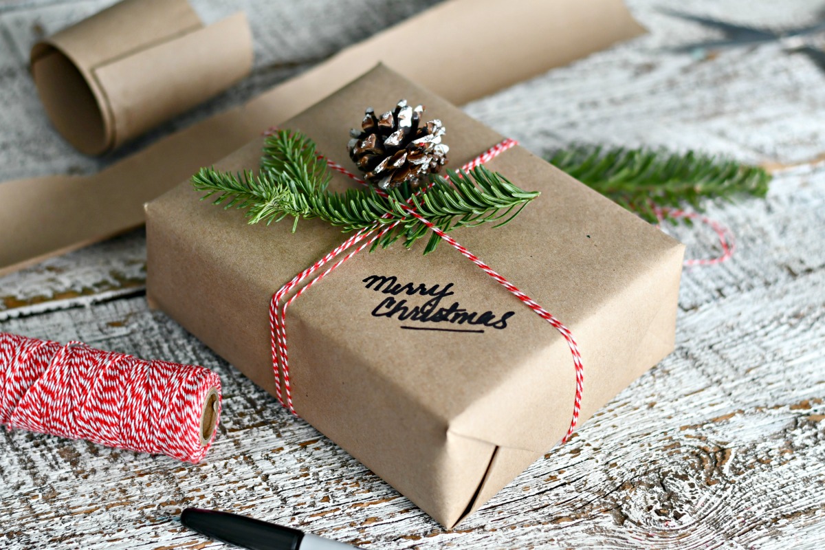 gift wrapped in brown paper, tied with twine, and decorated with pinecone and evergreen branch 
