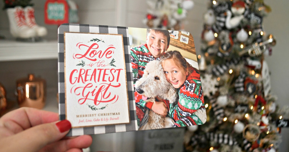 hand holding christmas card in front of christmas tree