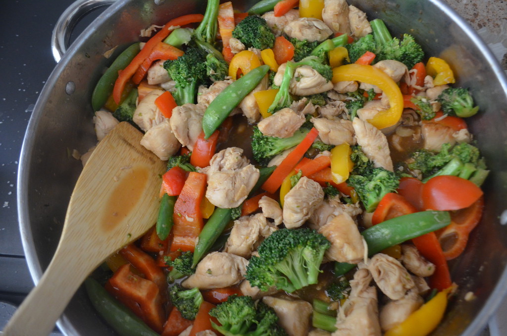 chicken stir fry with broccoli and bell peppers in pan with wood spoon