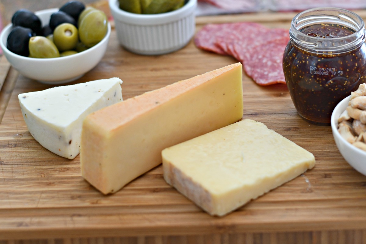 cheese, olives, jam, and meat on wooden cutting board