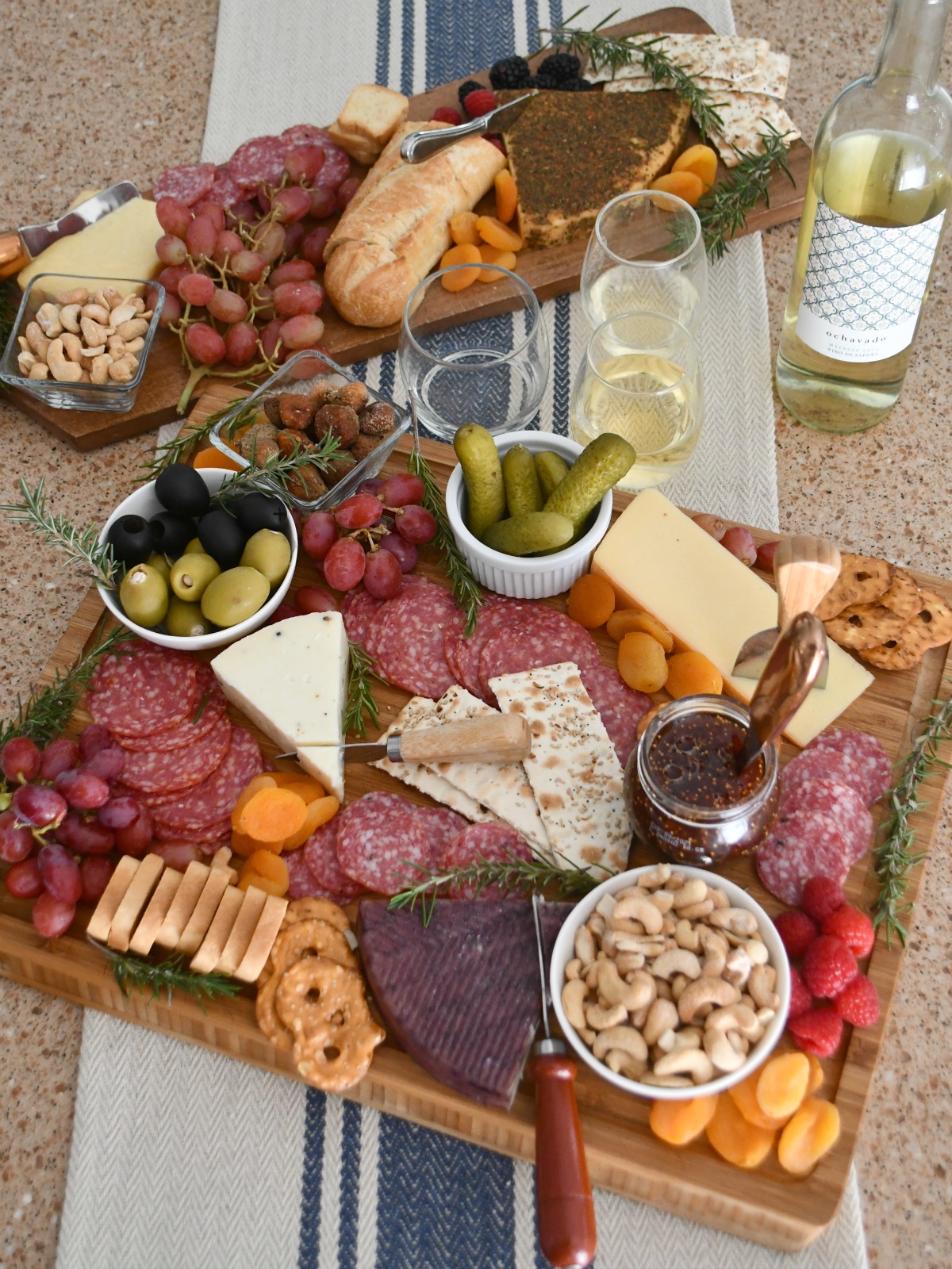 charcuterie boards with cheese assortment, wine, a bread loaf, glasses, and more