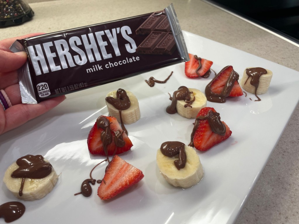 Woman using a Hershey bar to drizzle chocolate over fresh fruit which is one of our favorite kitchen hacks