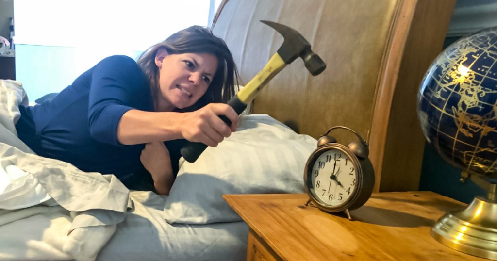 woman using a hammer to hit an alarm clock