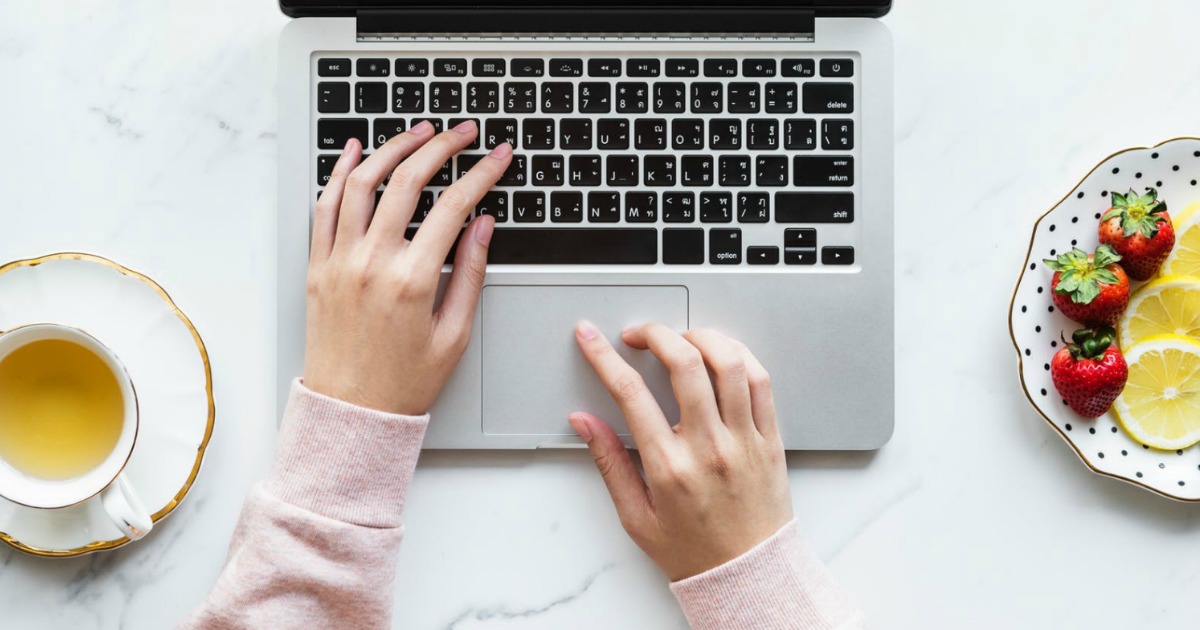 woman's hands pressing keys on laptop with coffee and fruit plate next to it