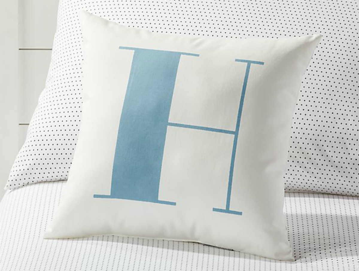 blue and white letter H pillow sitting on bed with sheets