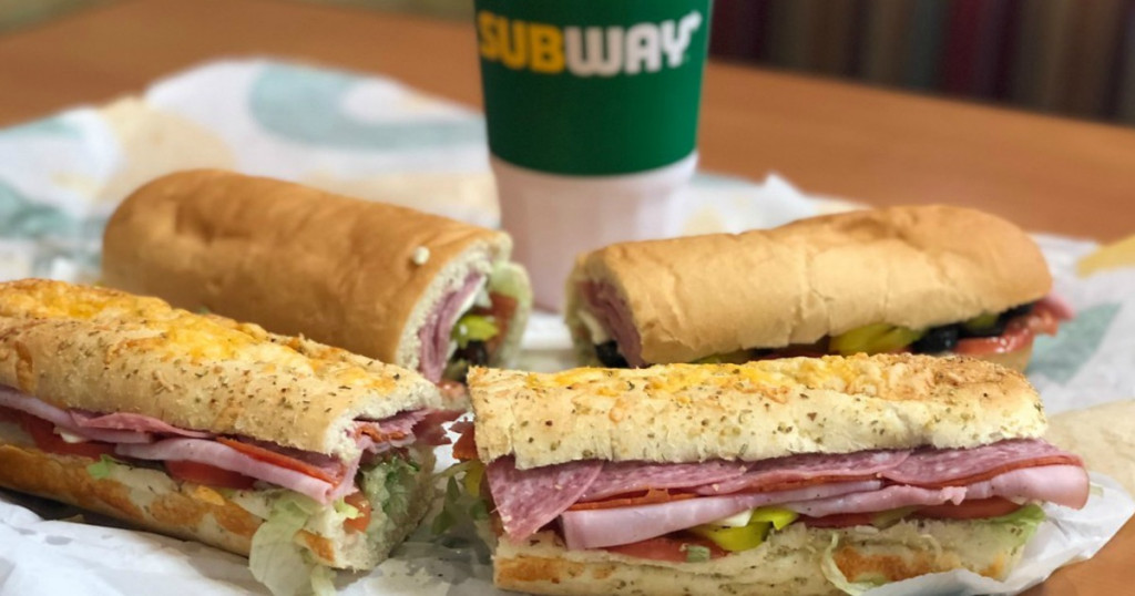 Two kinds of sub sandwiches on table, cut in half near drink