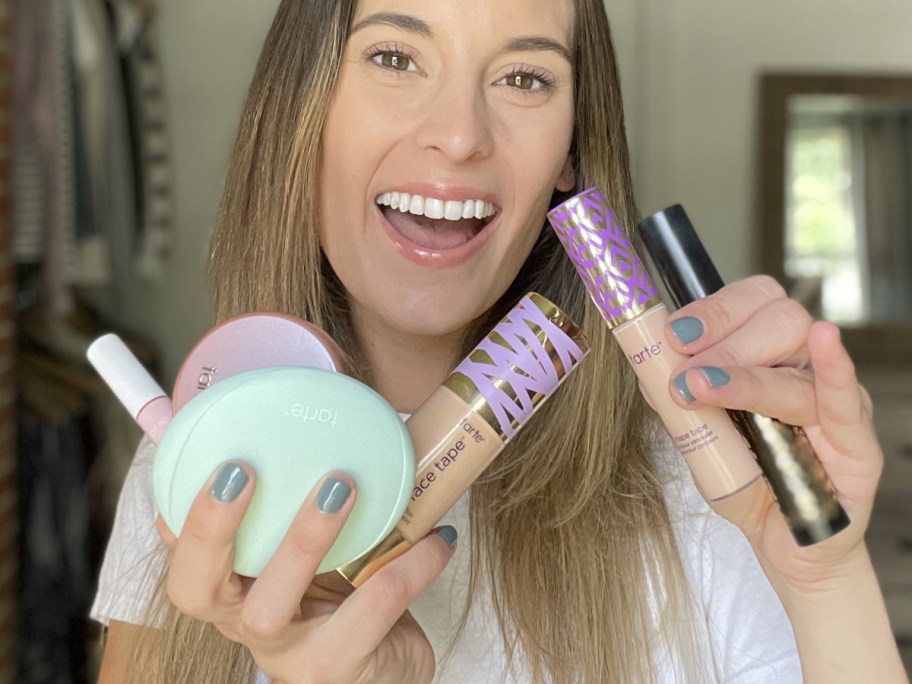 A woman holding a number of tarte cosmetic items