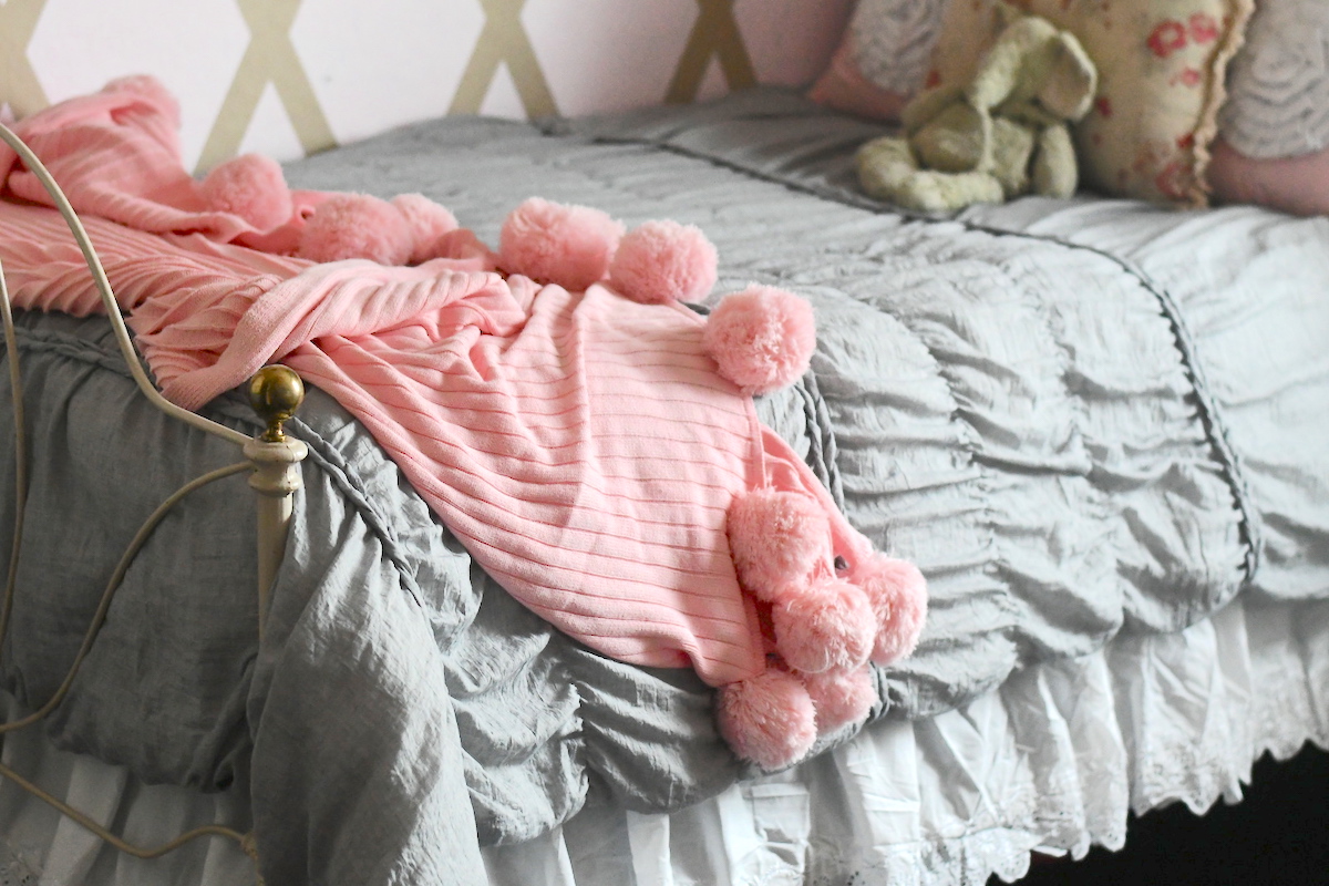 pink pom blanket laying on gray bed