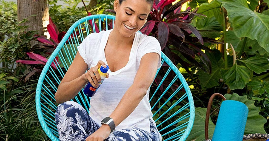 woman spraying herself with sunscreen