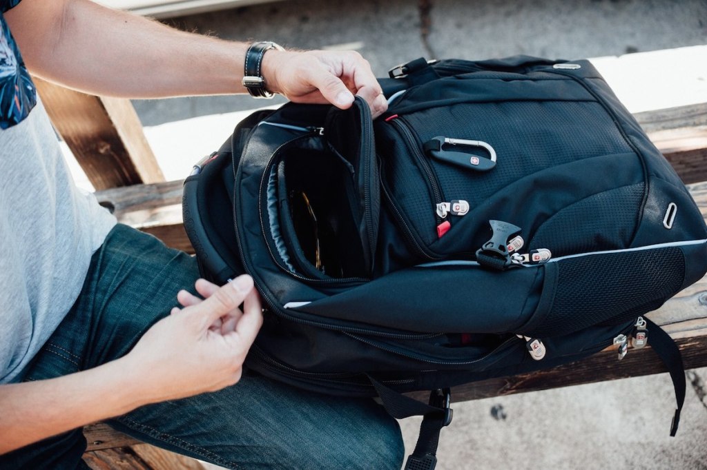 hands taking stuff out of black backpack sitting on bench