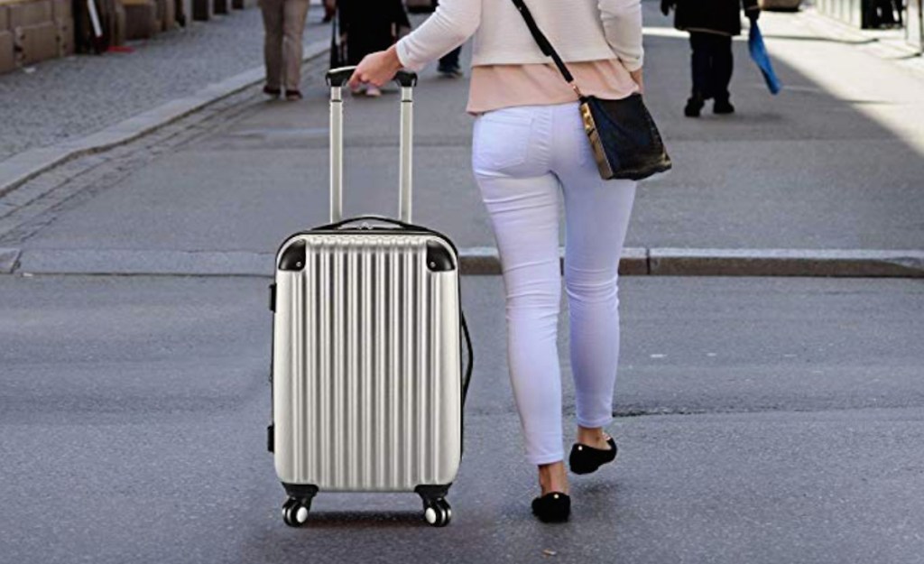 woman walking through city pulling silver luggage behind her