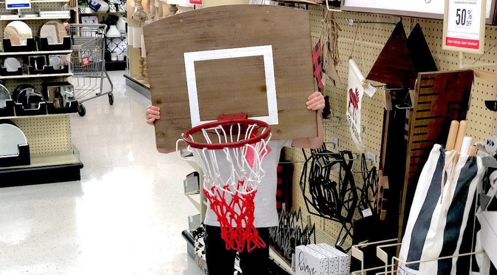 kid holding up a wooden basketball hoop in store aisle - kids decor themes hobby lobby