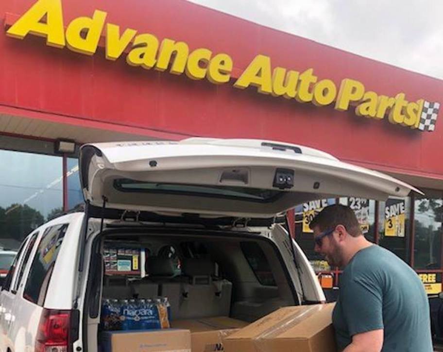 man putting boxes inside white car trunk with advance auto parts store sign in background