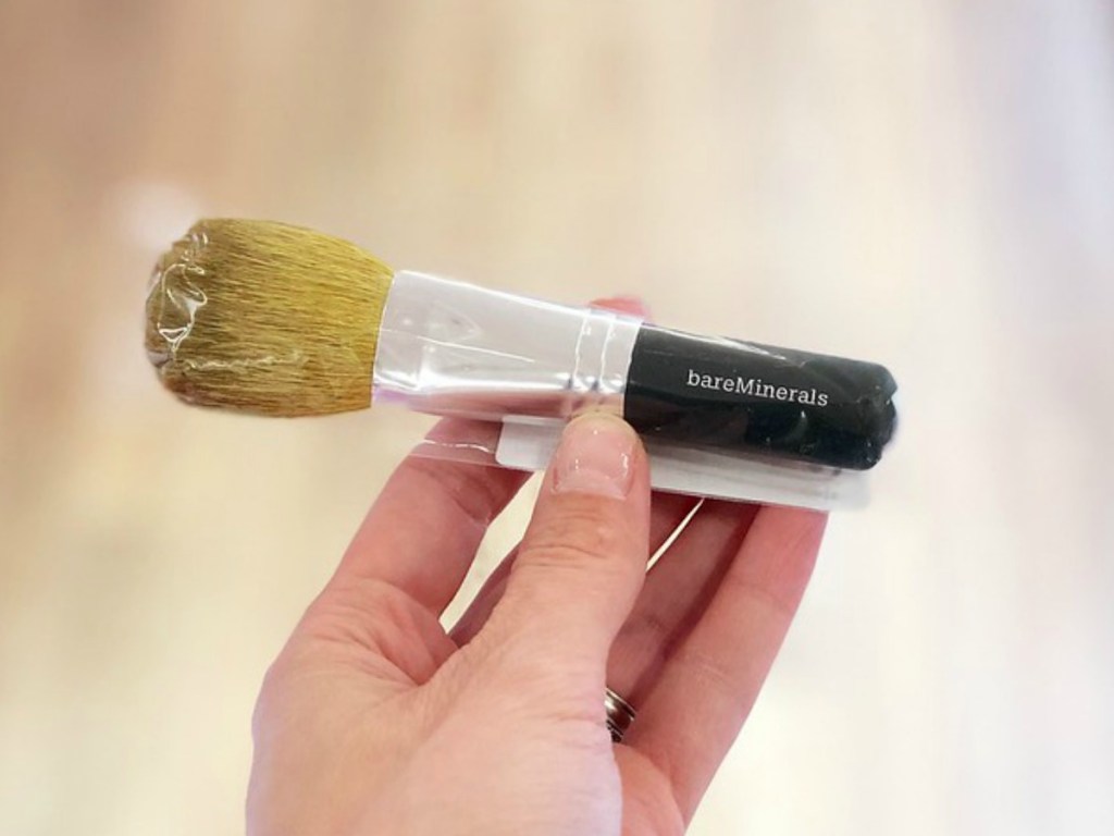 Hand holding bareMinerals makeup brush with blurred background