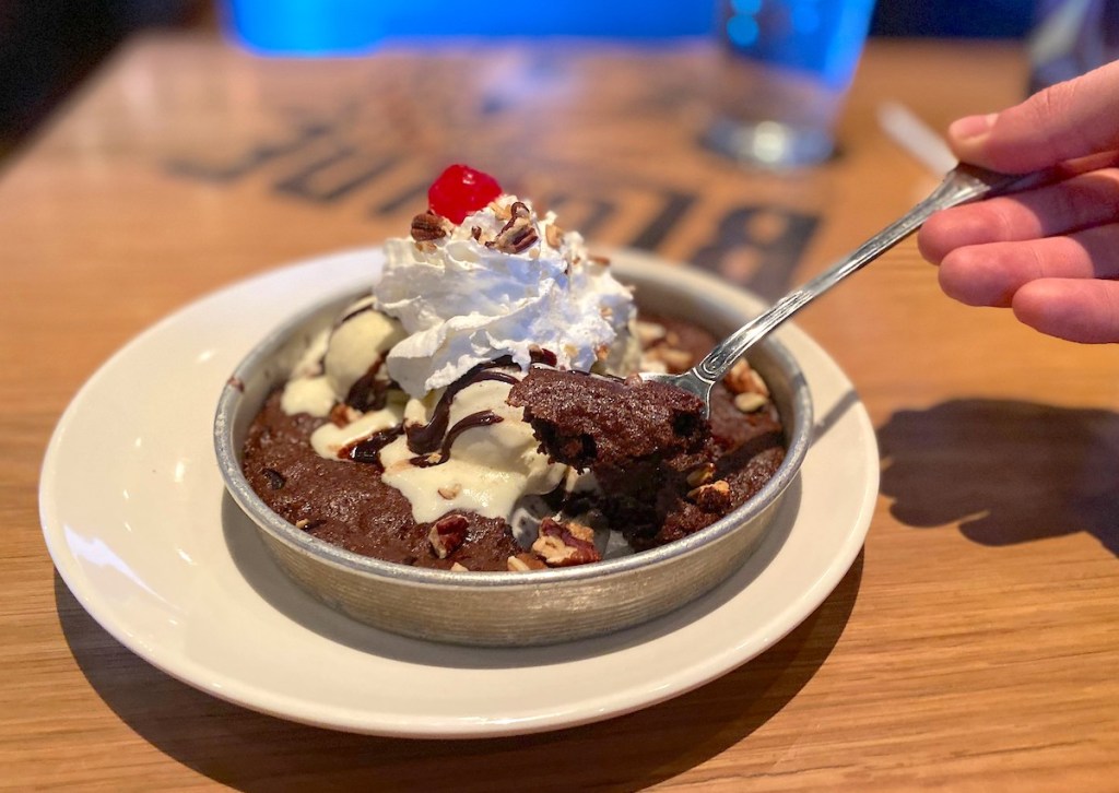 hand holding a fork full of deep dish cookie with whipped cream and cherry on top 