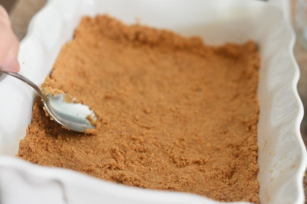 graham cracker crumbs being pressed into a dish with a spoon