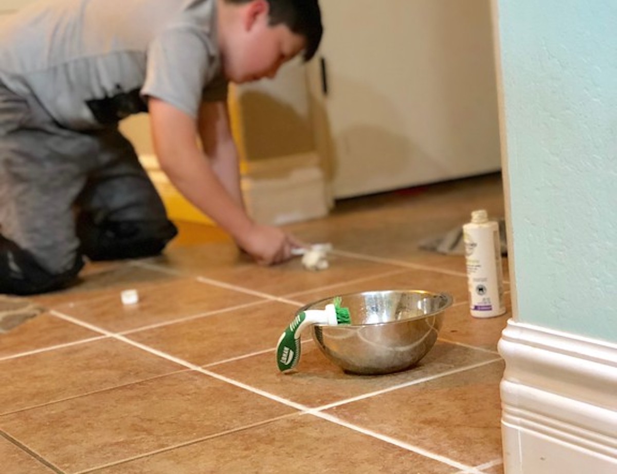 boy with toothbrush applying white grout sealant on tile floor