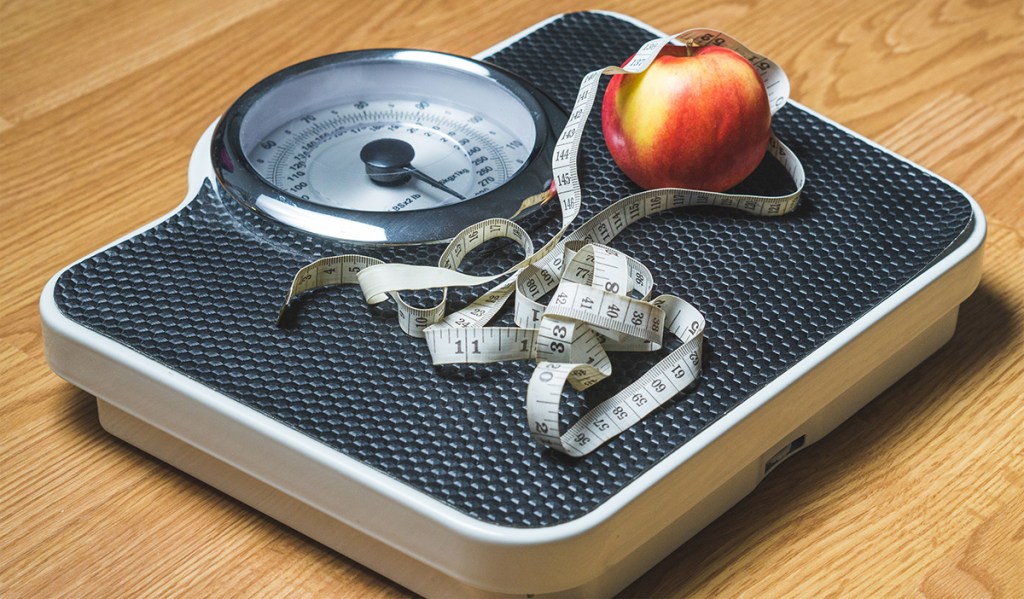 scale with apple and measuring tape on surface