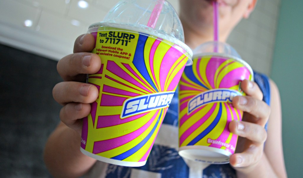boy holding two cups of slurpees with retro design on outside