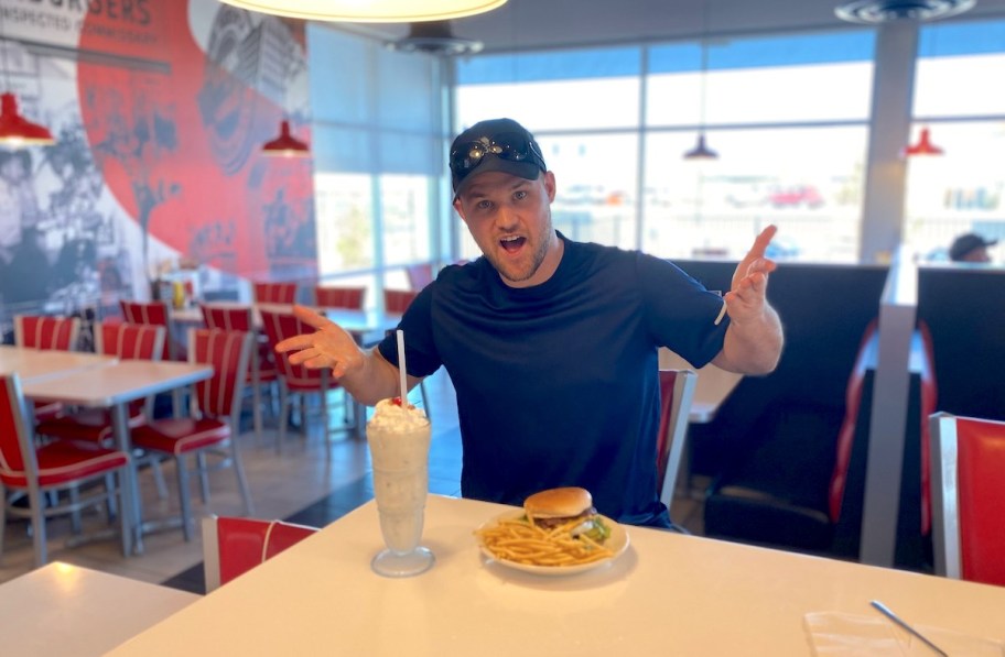 man sitting at table with milkshake burger and fries
