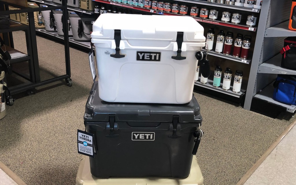 white yeti cooler stacked on top of black yeti cooler with tumblers on shelf in background