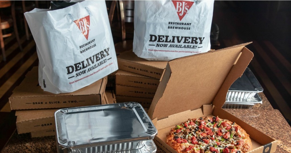 Bj's restaurant to-go bags next to catering pans and a pizza box with fresh pizza