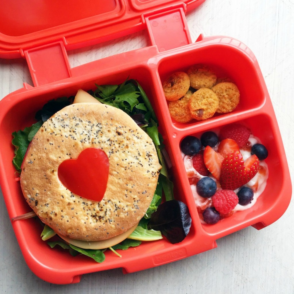 Bento box lunch container sandwich, crackers, berries, and yogurt.