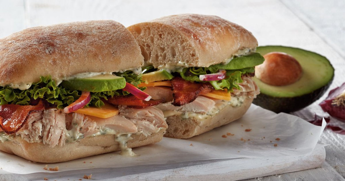 two halfs of boston market Chicken Avocado Club on ciabatta with half of an avocado with pit