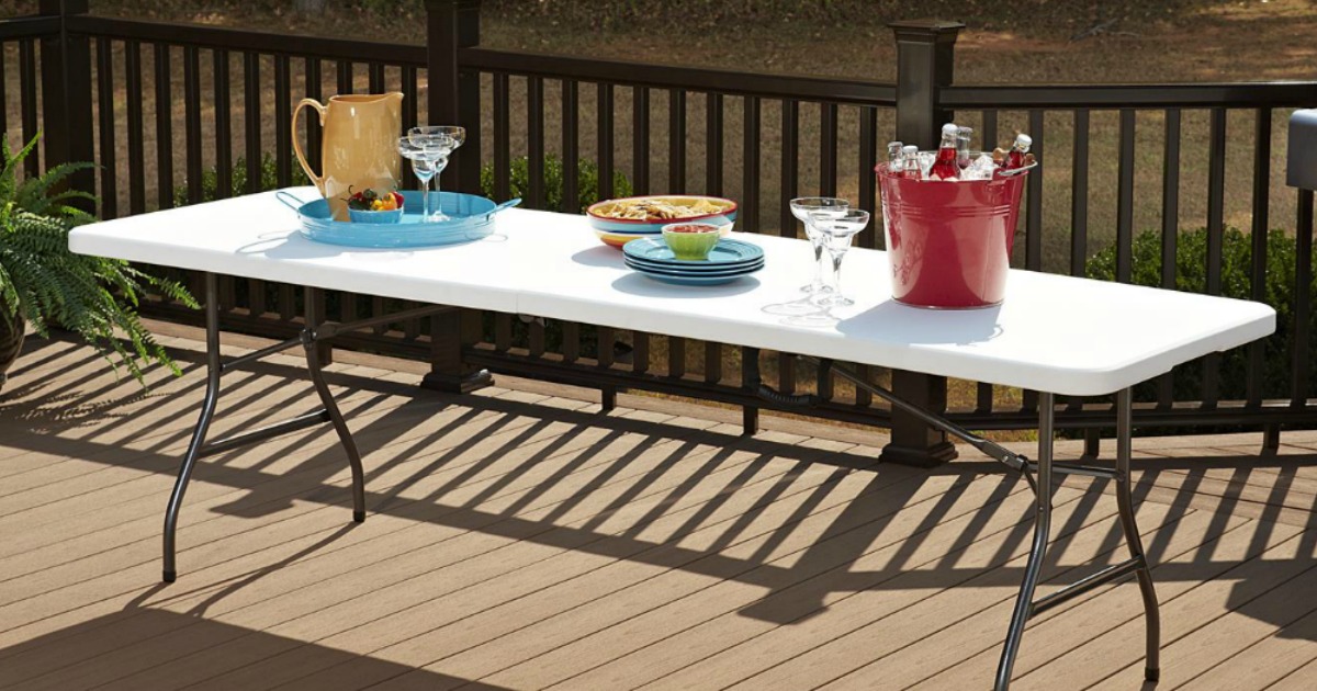 White table sitting on deck with food, drinks and plates on table