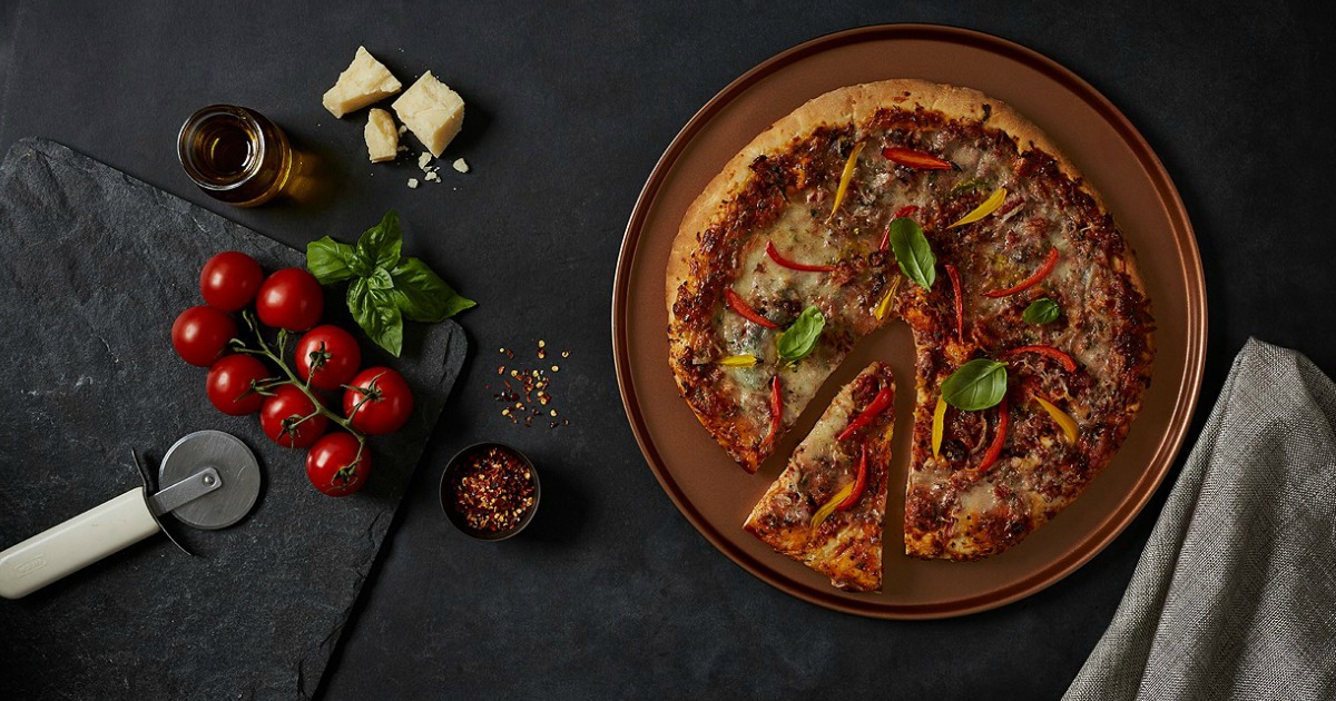 pizza pan holding pizza on a table with veggies and pizza cutter