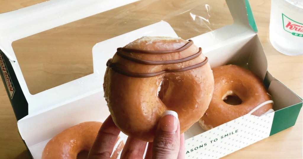 manicured hand holding krispy kreme doughnut