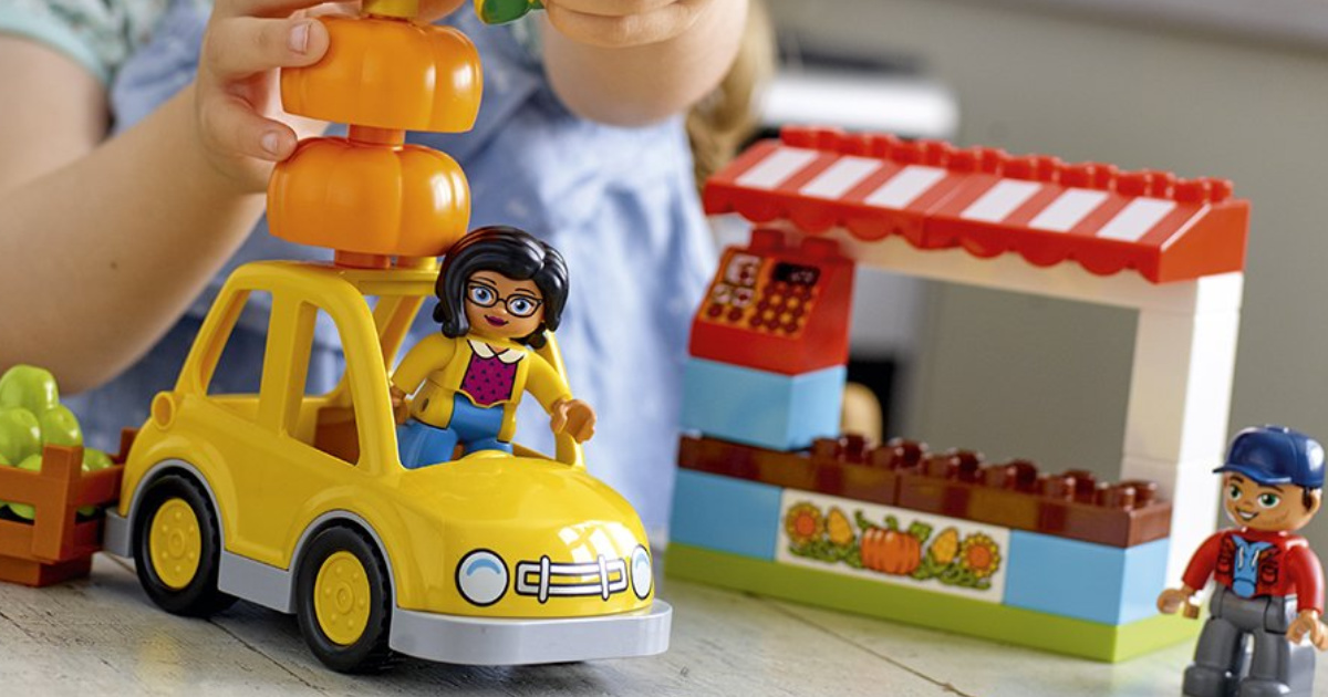 Little Girl Playing with a Yellow LEGO Car with a Fruit Stand