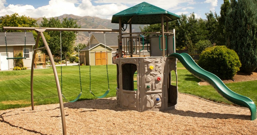 Large playset with a tower, swings, trapeze swing on a playground with bark