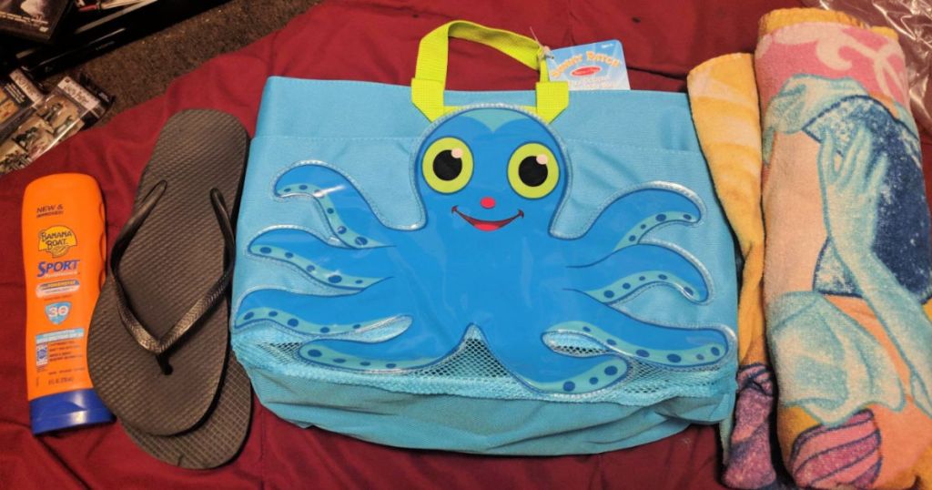 Melissa & Doug Sunny Patch Flex Octopus Large Beach Tote Bag With Mesh Panels on bed next to black sandals, sun screen, and towel