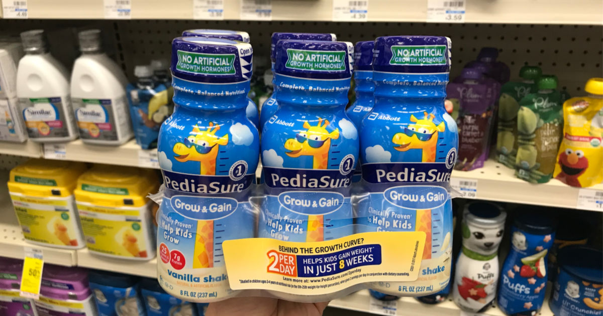 Hand holding pediasure in front of shelf