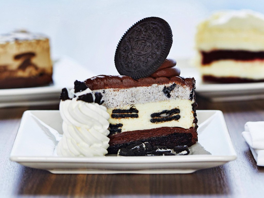 The Cheesecake Factory Oreo Cheesecake on plate with whipped cream and assorted cheesecake in the background