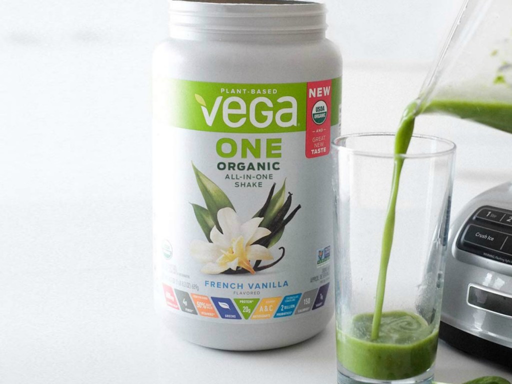 vega one french vanilla protein powder canister sitting on counter by blender pouring a shake into a cup