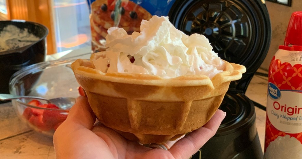 hand holding waffle bowl with whipped cream inside of it