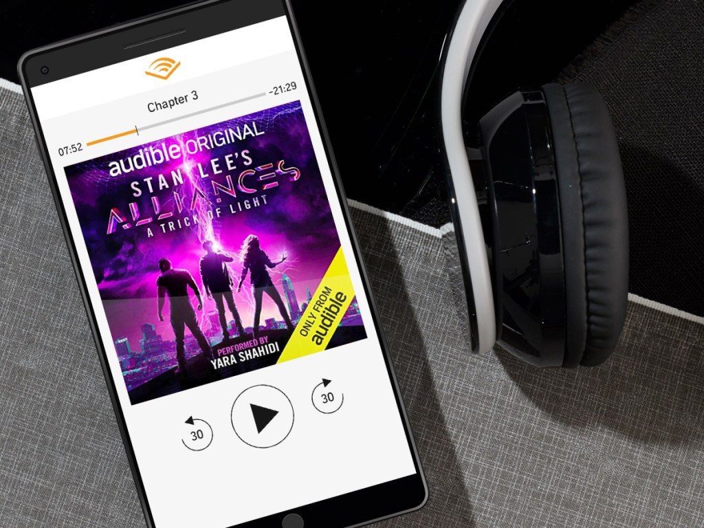 image of phone playing Stan Lee's Alliances: A Trick of Light with headphones next to it