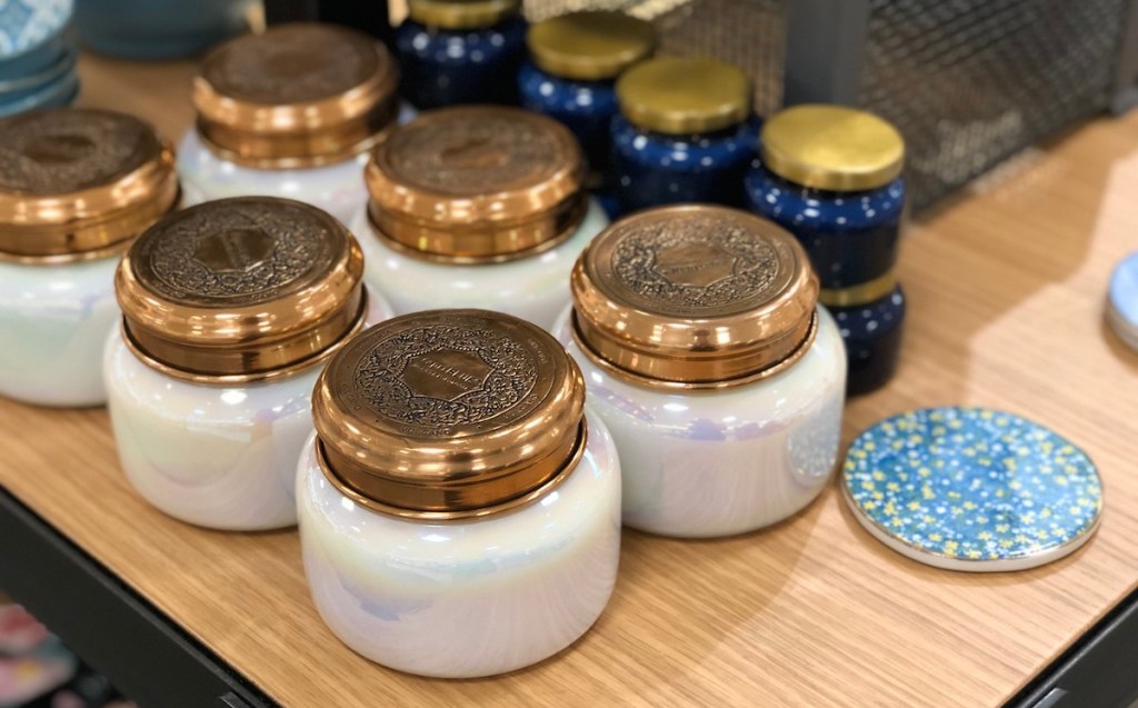 large white and gold Capri Blue candles on wood table with small blue mini candles