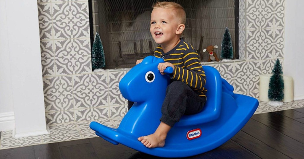 little boy on blue rocking horse in front of fireplace