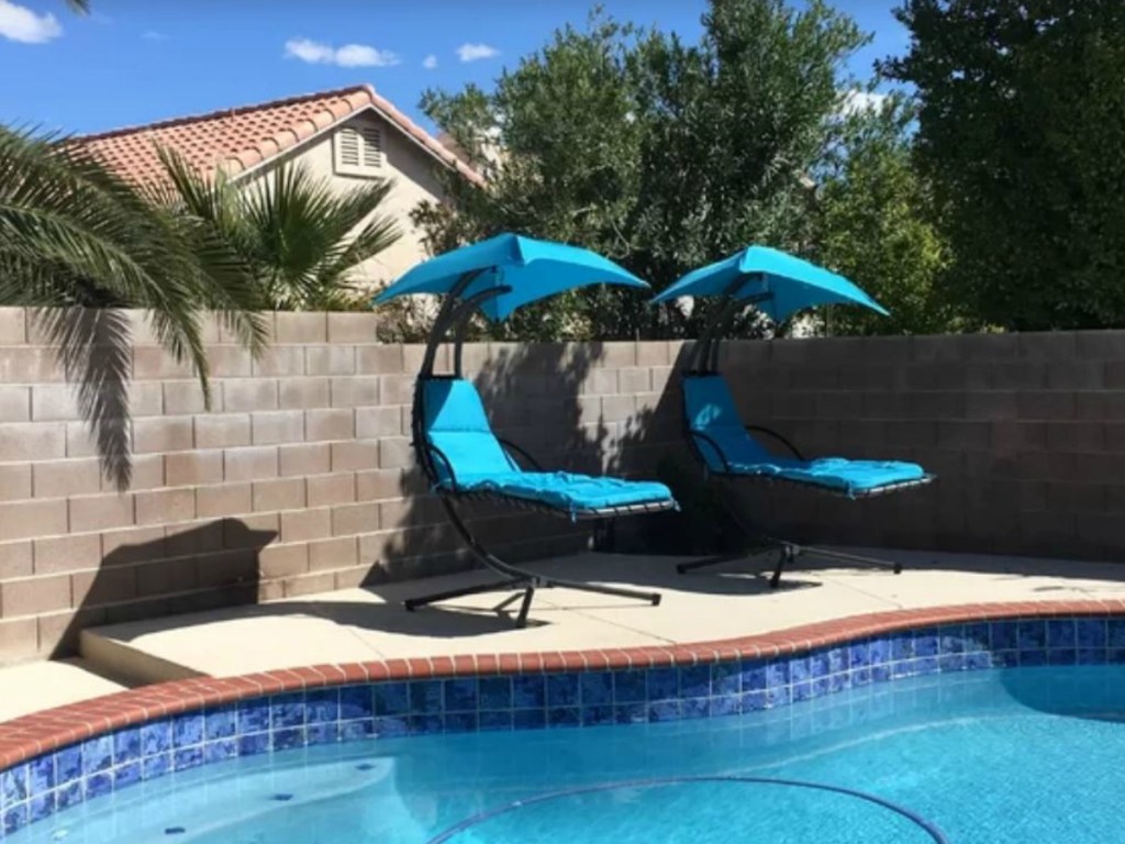 two blue chairs with sun shades next to a pool