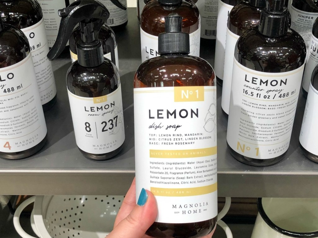 Manicured hand holding lemon dish soap in front of other Magnolia cleaning products